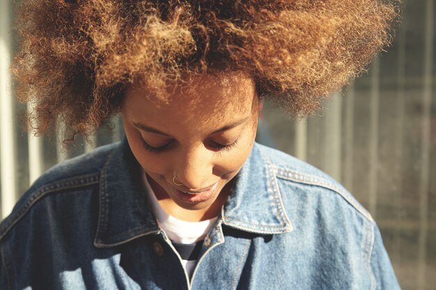 Hermosa joven africana con cabello rizado y piel limpia y saludable posando al aire libre en la pared gris