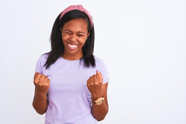 Hermosa joven afroamericana con una diadema sobre un fondo aislado muy feliz y emocionada haciendo el gesto de ganador con los brazos levantados sonriendo y gritando por el éxito Concepto de celebración