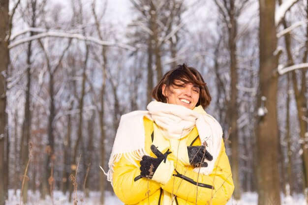 Hermosa joven alegre en un bosque de invierno paisaje nevado divirtiéndose se regocija en invierno y nieve en ropa de abrigo