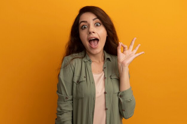 Hermosa joven alegre con camiseta verde oliva que muestra un gesto bien aislado en la pared amarilla