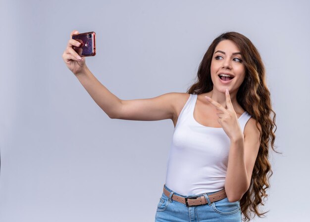 Hermosa joven alegre haciendo el signo de la paz y tomando selfie