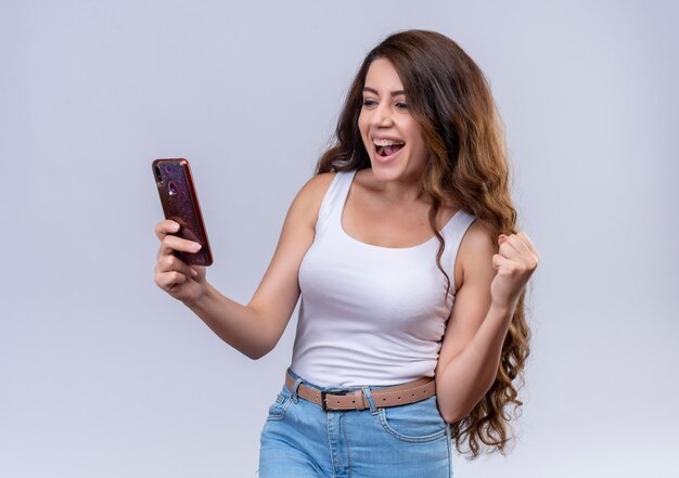 Hermosa joven alegre mirando el teléfono móvil con el puño levantado