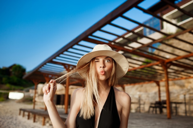 Hermosa joven alegre en sombrero haciendo cara graciosa en la playa de la mañana