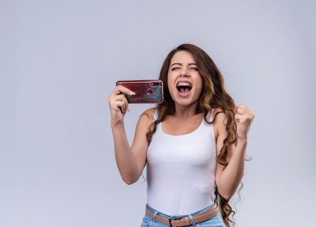 Hermosa joven alegre sosteniendo el teléfono móvil y levantando el puño con los ojos cerrados con espacio de copia