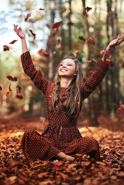 Hermosa joven arrojando hojas en el bosque de otoño