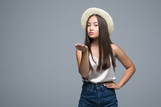 Hermosa joven asiática soplar un beso sobre fondo gris