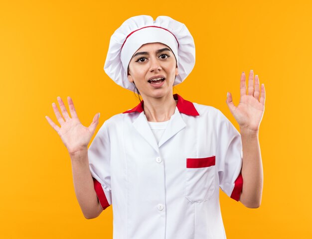 Hermosa joven asustada en uniforme de chef mostrando gesto de parada