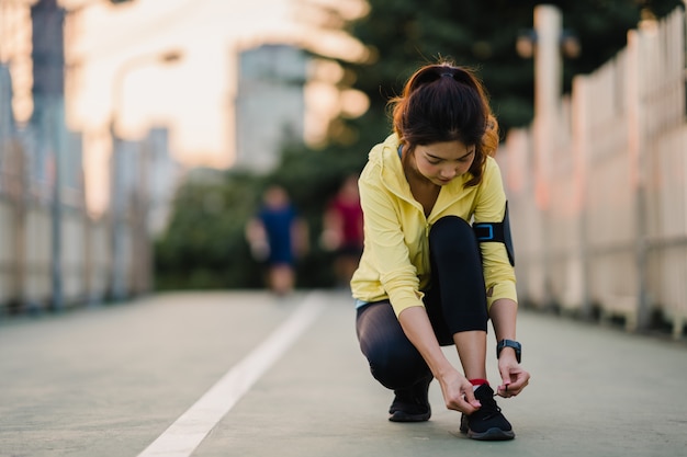 Hermosa joven atleta asiática ejercicios de señora atar cordones para hacer ejercicio en el entorno urbano. Chica adolescente japonesa vistiendo ropa deportiva en puente de pasarela en la mañana temprano. Estilo de vida activo deportivo en la ciudad.