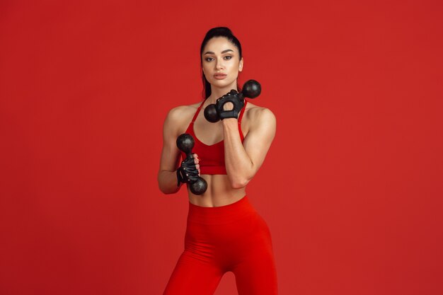 Hermosa joven atleta practicando en la pared roja del estudio