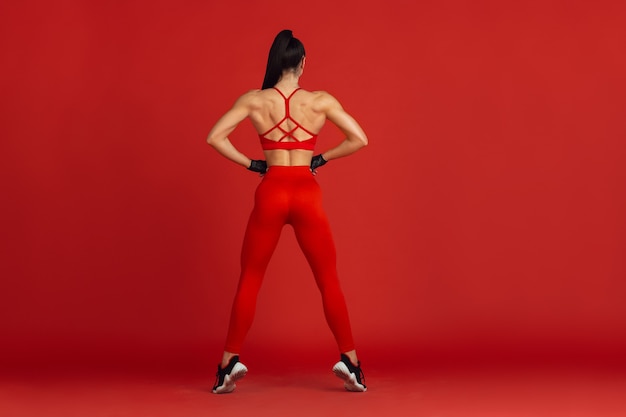 Hermosa joven atleta practicando en la pared roja del estudio