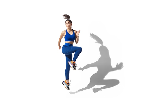 Foto gratuita hermosa joven atleta practicando sobre fondo blanco de estudio, retrato con sombras. modelo de ajuste deportivo en movimiento y acción.