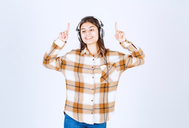 Hermosa joven en auriculares escuchando canciones sobre pared blanca.