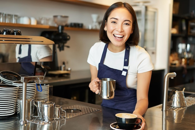 Hermosa joven barista haciendo capuchino vertiendo leche al vapor para latte art en taza darte