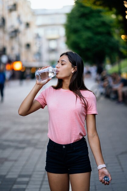 Hermosa joven bebe con una botella de agua en una calle de la ciudad