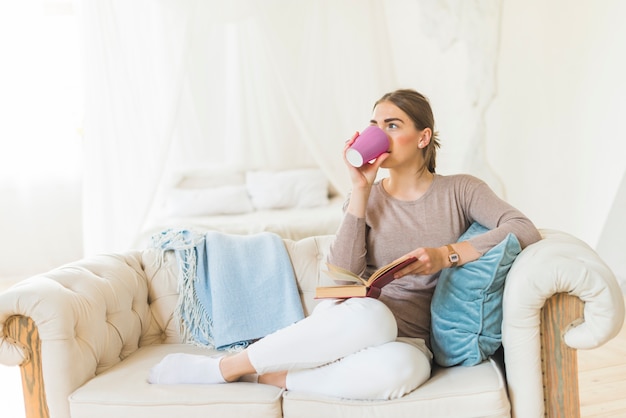 Hermosa joven bebiendo café mientras sostiene el libro