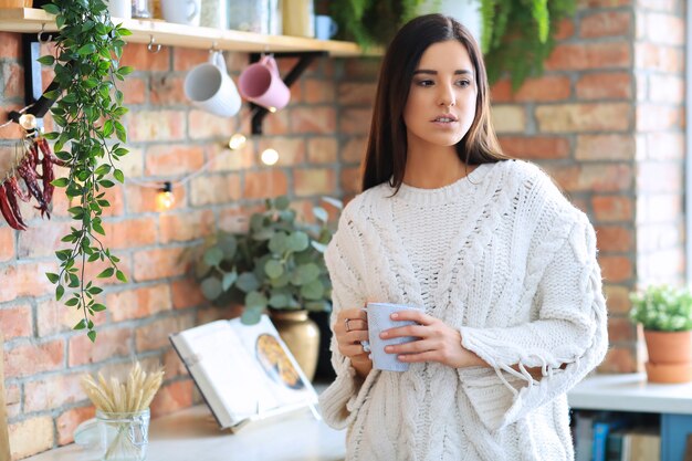 Hermosa joven bebiendo café o té en la cocina