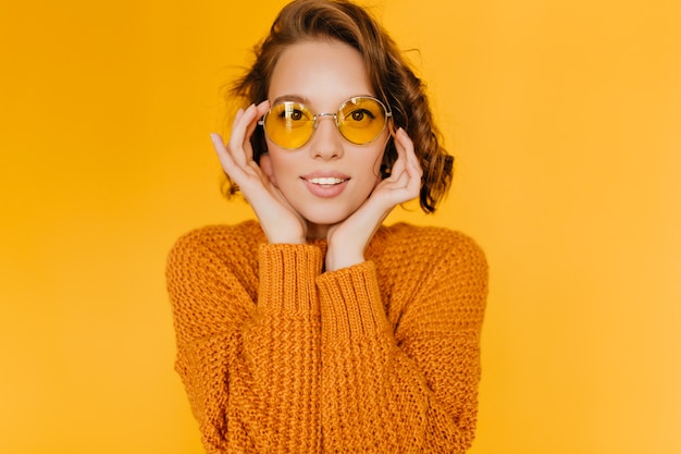 Hermosa joven blanca en suéter de moda apuntando la cara con las manos y mirando con interés