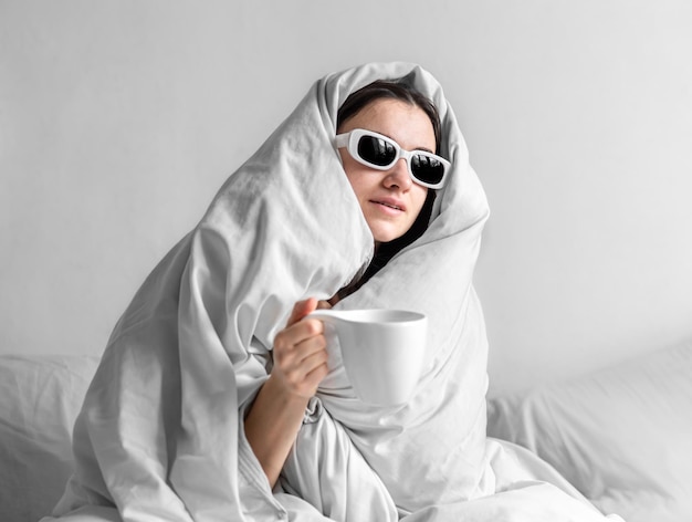 Foto gratuita una hermosa joven en una cama blanca con una taza de café.