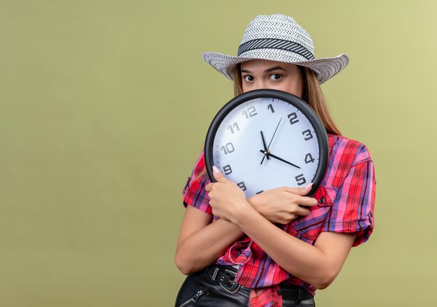 Una hermosa joven en una camisa a cuadros con reloj de pared