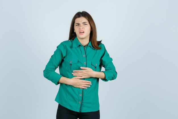 Foto gratuita hermosa joven en camisa verde sintiendo dolor de estómago y luciendo mal, vista frontal.