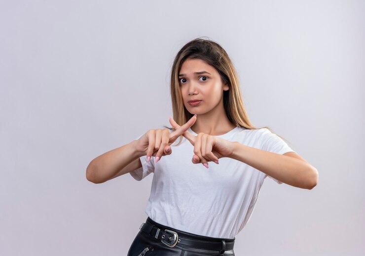 Foto gratuito una hermosa joven en camiseta blanca mostrando cruzar los dedos formando una x en una pared blanca