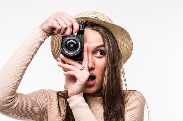 Hermosa joven en camiseta brillante y sombrero hace foto en retrocamera aislado en blanco