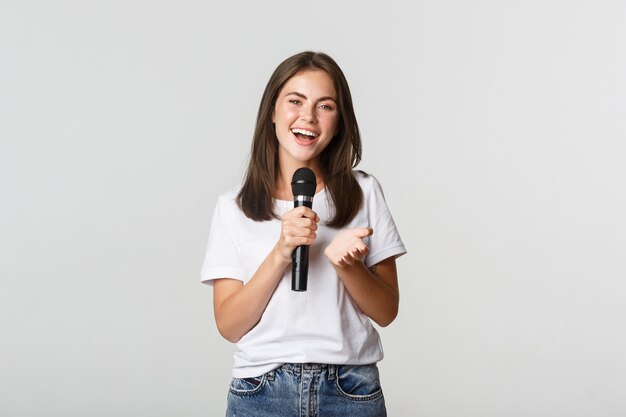 Hermosa joven cantando una canción en el micrófono en el karaoke, de pie en blanco.