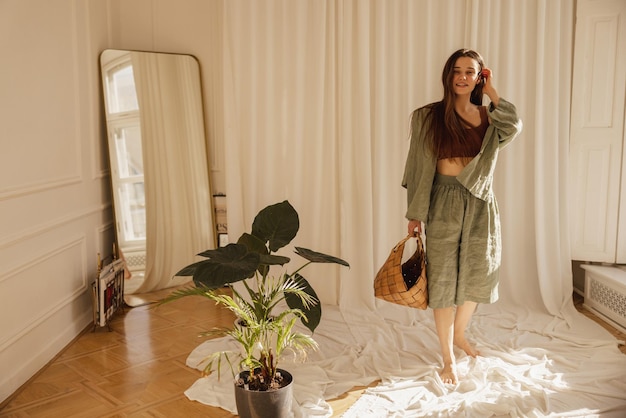 Hermosa joven caucásica se mete el pelo detrás de la oreja mientras está de pie en el interior de la sala de luz Morena viste ropa informal de verano y sostiene una bolsa Estilo de vida diferentes emociones concepto de ocio