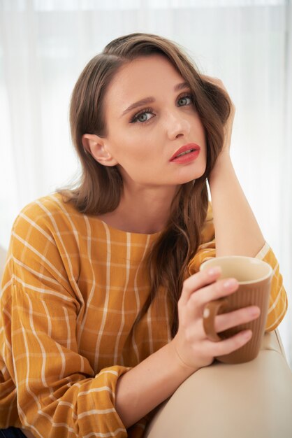 Hermosa joven caucásica posando en casa en el sofá con una taza de café