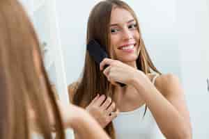 Foto gratuita hermosa joven cepillando su largo cabello delante de su espejo.