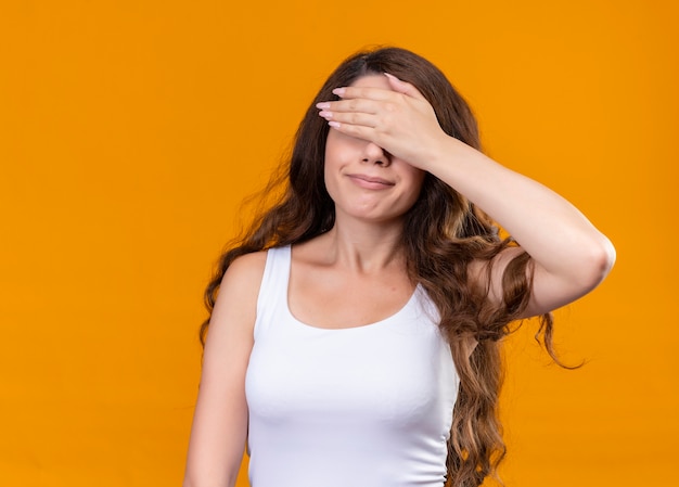 Hermosa joven cerrando los ojos con la mano en la pared naranja aislada con espacio de copia