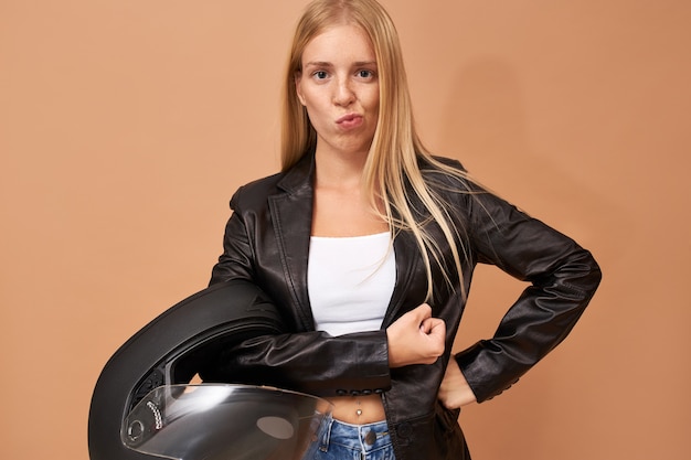 Hermosa joven ciclista mujer rubia de moda con elegante chaqueta de cuero negro con expresión facial segura