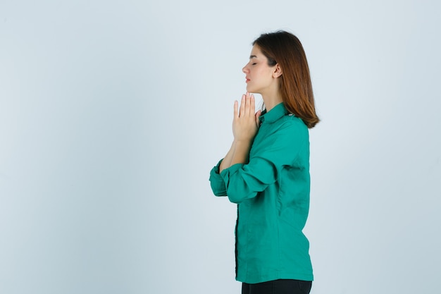 Hermosa joven cogidos de la mano en gesto de oración en camisa verde y mirando esperanzado. .