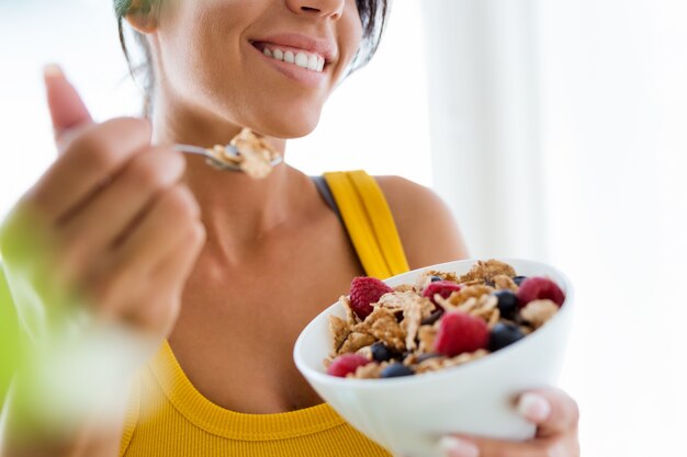 Hermosa joven comiendo cereales y frutas en casa.