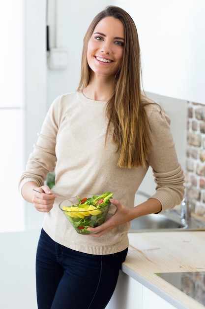 Hermosa joven comiendo ensalada de frutas en la cocina.