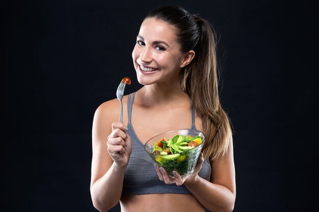 Hermosa joven comiendo ensalada sobre fondo negro.