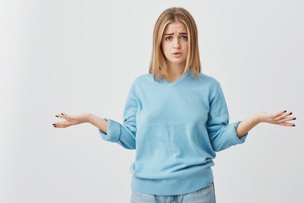 Hermosa joven confundida y confundida vestida casualmente exclamando desesperada y encogiéndose de hombros con total incredulidad después de recibir algunas noticias negativas inesperadas. Lenguaje corporal