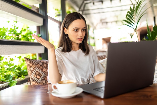 Hermosa joven confundida usando laptop en cafe