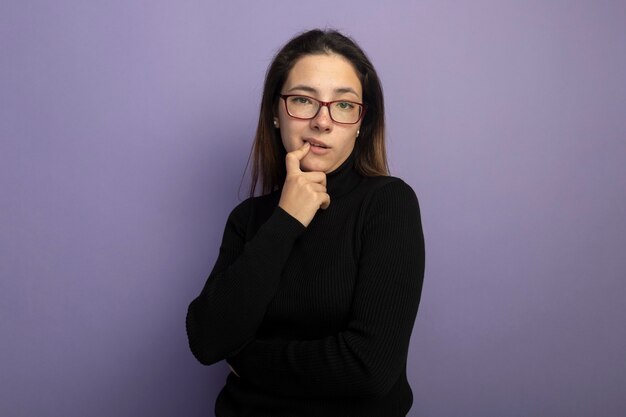 Hermosa joven en un cuello alto negro y gafas desconcertado