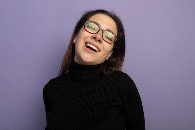 Hermosa joven en un cuello alto negro y gafas sonriendo alegremente