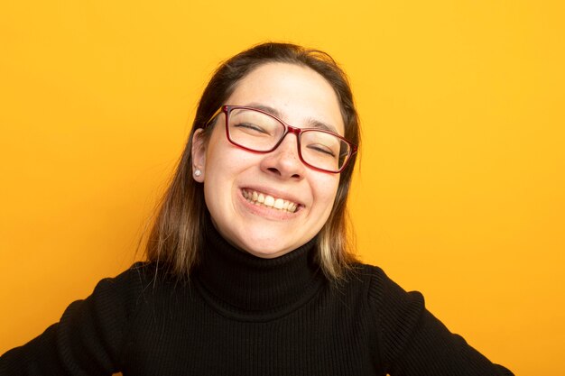 Hermosa joven en un cuello alto negro y gafas sonriendo ampliamente