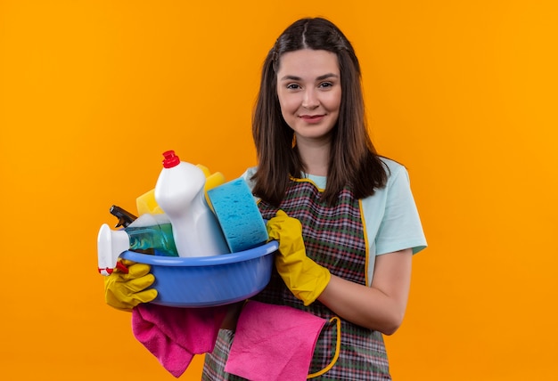 Foto gratuita hermosa joven en delantal y guantes de goma con lavabo con herramientas de limpieza sonriendo amable mirando a la cámara