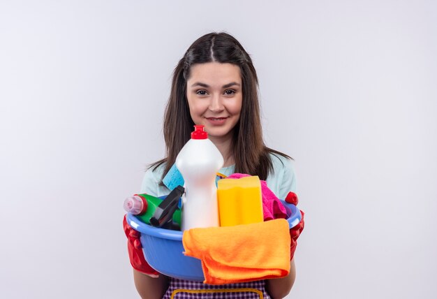 Hermosa joven en delantal y guantes de goma con lavabo con herramientas de limpieza sonriendo confiado