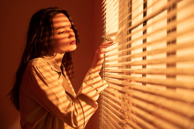 Hermosa joven detrás de las persianas de la ventana