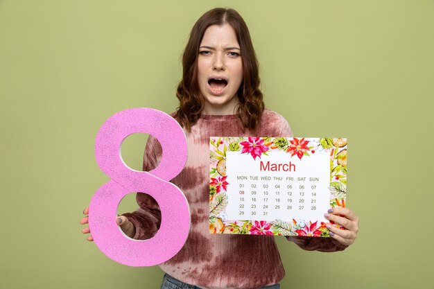 Hermosa joven disgustada en el día de la mujer feliz sosteniendo el número ocho con calendario