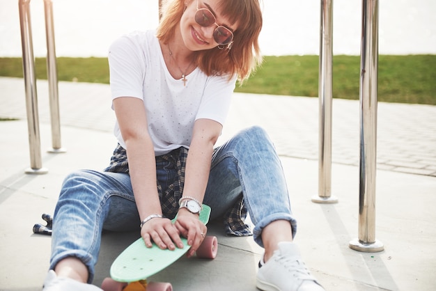 Una hermosa joven se divierte en el parque y monta una patineta.