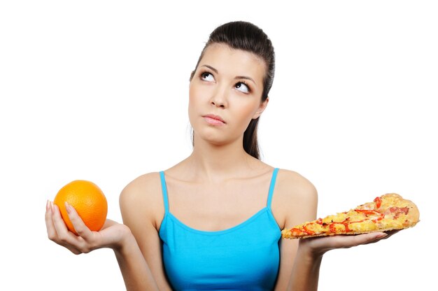 Hermosa joven eligiendo entre pizza y naranja