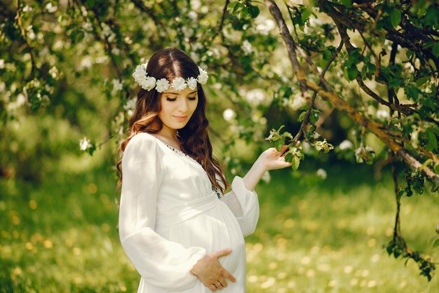 hermosa joven embarazada en un vestido blanco largo y corona sobre su cabeza