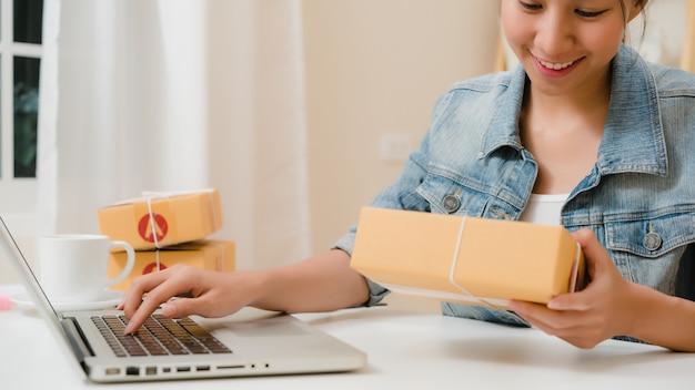 Hermosa joven empresaria asiática inteligente, dueña de una mujer de negocios en línea que comprueba el producto en stock y la guarda en el equipo que trabaja en casa.