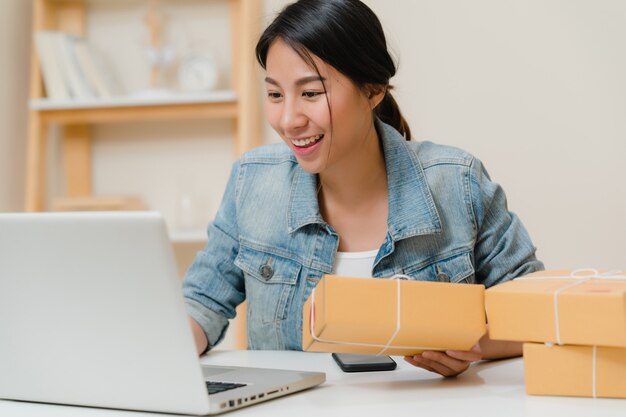 Hermosa joven empresaria asiática inteligente, dueña de una mujer de negocios en línea que comprueba el producto en stock y la guarda en el equipo que trabaja en casa.